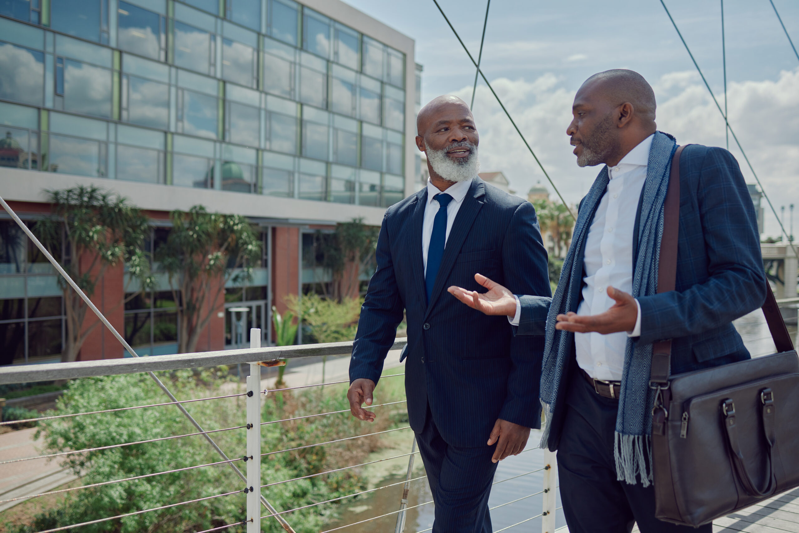 african men in city, business team and discussion with travel, partnership and commute to work. communication, black male people in collaboration and walking on urban bridge with journey to office